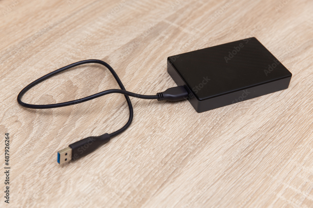 External hard drive with cable on a wooden table External hard drive with cable on a wooden table