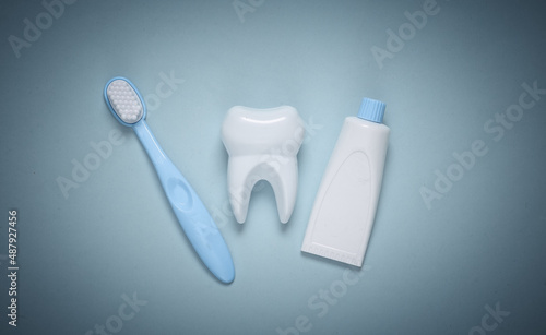 Fake tooth, toothbrush and toothpaste on blue background. Top view
