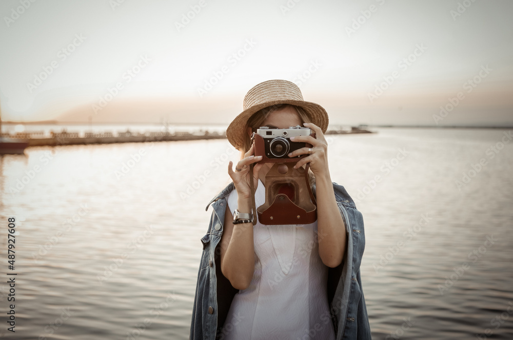 Young woman takes a photo on camera at sunrise on the sea. Travel and tourism concept