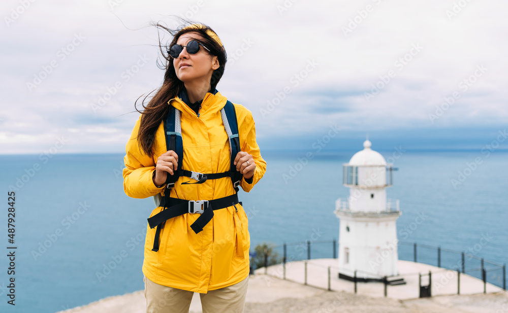 Traveler with his tourist backpack is standing against a sea background. Travel, tourism and active lifestyle concept. Portrait of a female traveler on the background of the blue sea. Copy space