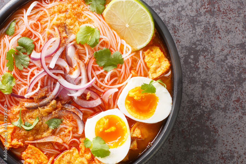 Mohinga is a rice noodle and fish soup from Myanmar and an essential part of Burmese cuisine closeup in the bowl on the table. Horizontal top view from above Mohinga is a rice noodle and fish soup from Myanmar and an essential part of Burmese cuisine closeup in the bowl on the table. Horizontal top view from above