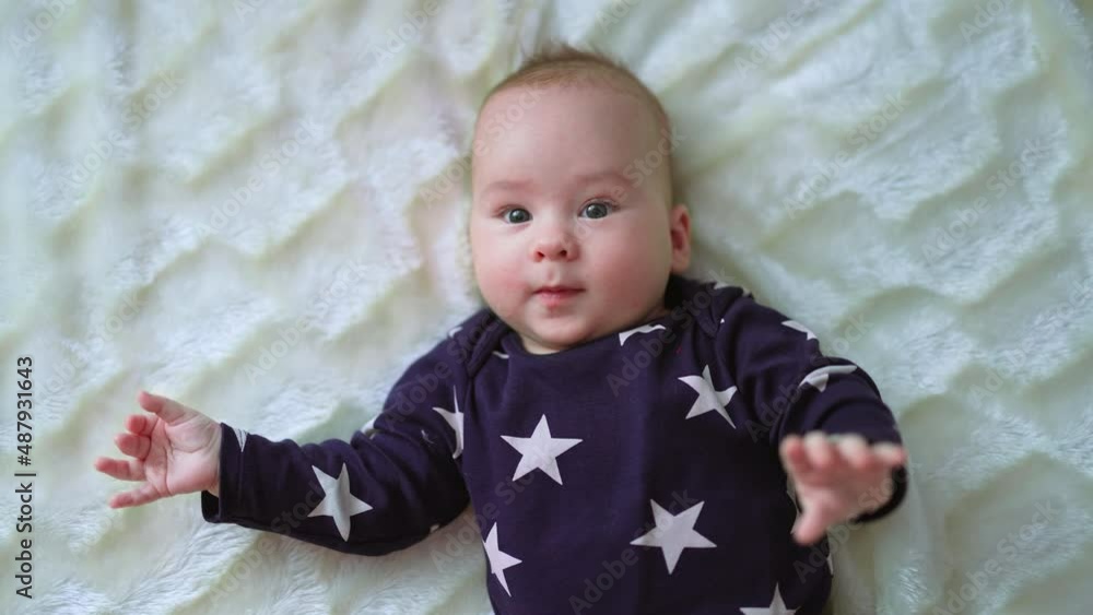 Healthy active infant boy freezes for a moment and looks straight ahead. Beautiful baby smiling slightly lying on white bed. Close up. Healthy active infant boy freezes for a moment and looks straight ahead. Beautiful baby smiling slightly lying on white bed. Close up.