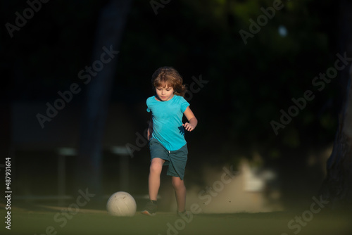 Child playing football on the playground in park. Boy child kicking football on the sports field during. © Volodymyr
