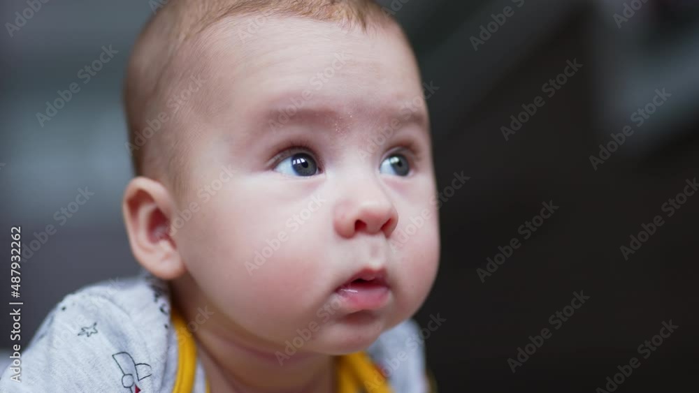 Beautiful face of a small Caucasian infant boy lying on his belly. Cute baby looking around with surprise. Close up. Blurred backdrop. Beautiful face of a small Caucasian infant boy lying on his belly. Cute baby looking around with surprise. Close up. Blurred backdrop.
