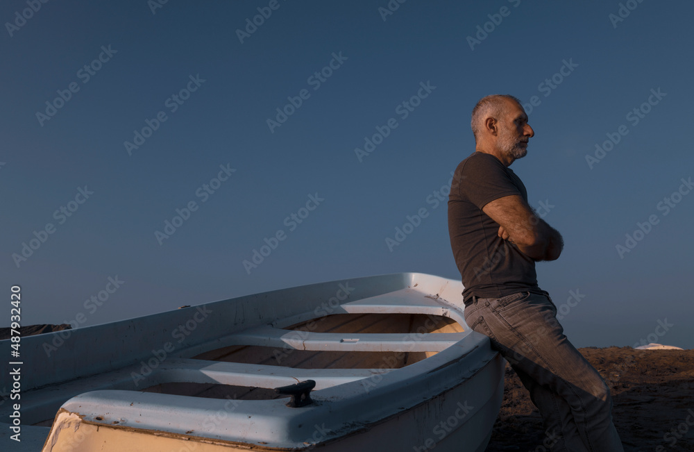 Adult man standing on beach with fishing boat during sunset. Almeria, Spain