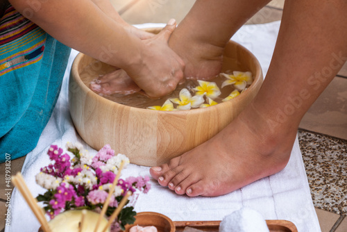 Feet, young women wash their feet in a wooden tub with frangipani flowers for a foot spa. 