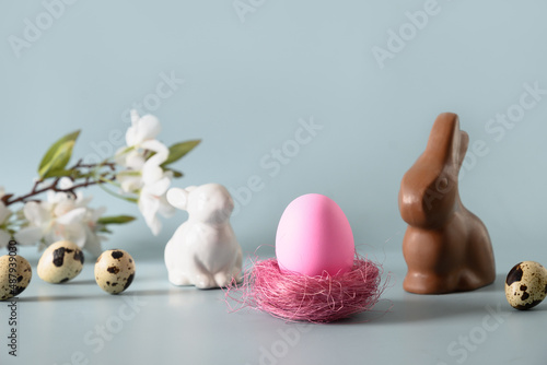 Easter pink egg in nest and chocolate bunny in spring composition on blue background. Happy Easter greeting card.
