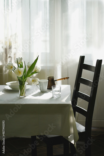 A bouquet of tulips on the table, white dishes, the table is covered with a white tablecloth.
