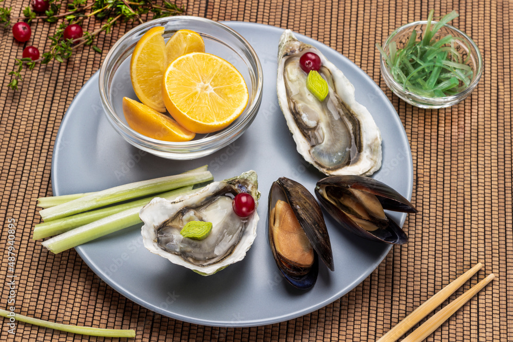 Open shells of oysters and mussels, bowl of lemon on gray plate. Open shells of oysters and mussels, bowl of lemon on gray plate.
