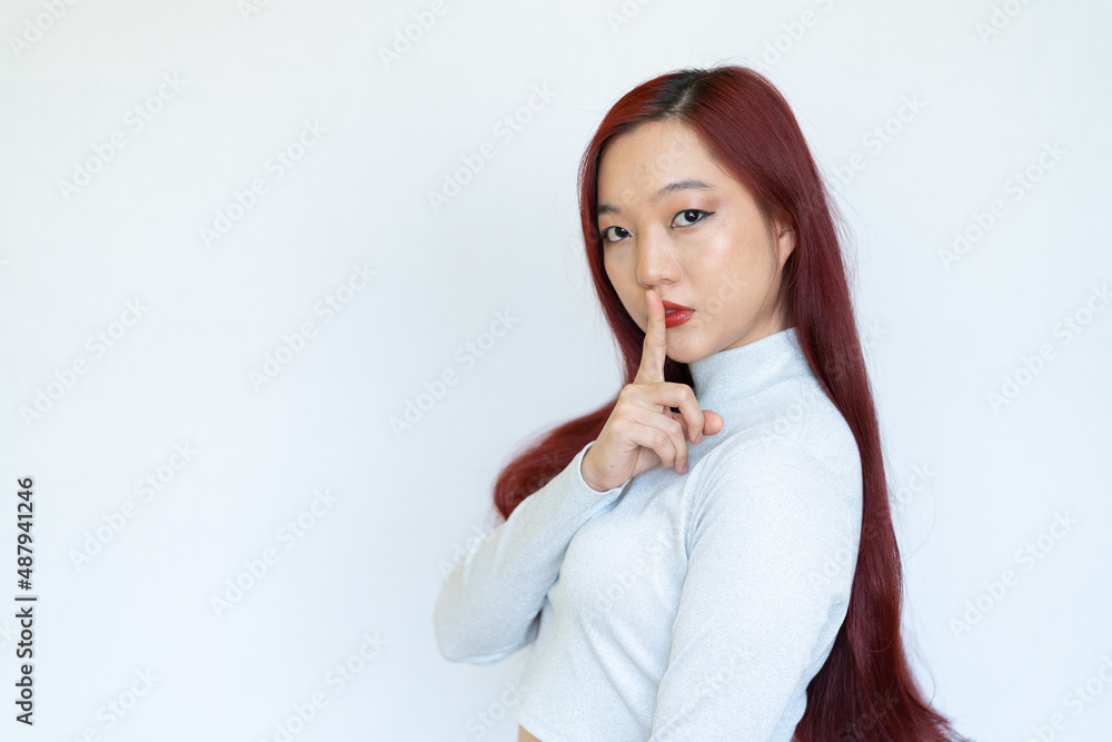 Pretty charming young woman having secret while holding finger on lips and showing silence sign while standing on white background Pretty charming young woman having secret while holding finger on lips and showing silence sign while standing on white background