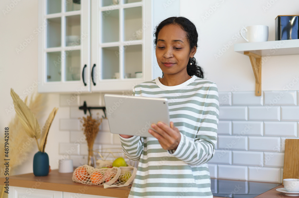 African-american female using digital device in kitchen. Searching recipe before starting cooking African-american female using digital device in kitchen. Searching recipe before starting cooking
