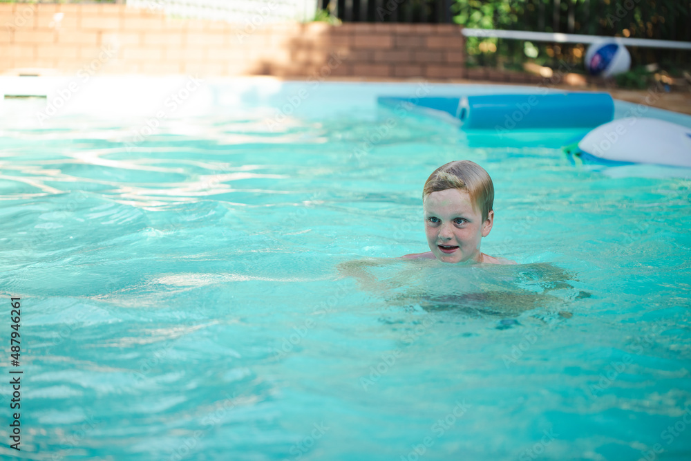 Happy pre-teen boy swimming in backyard pool