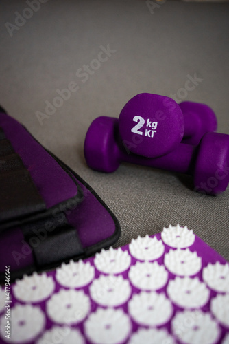 mat with spikes, dumbbells and weights for legs on a gray background