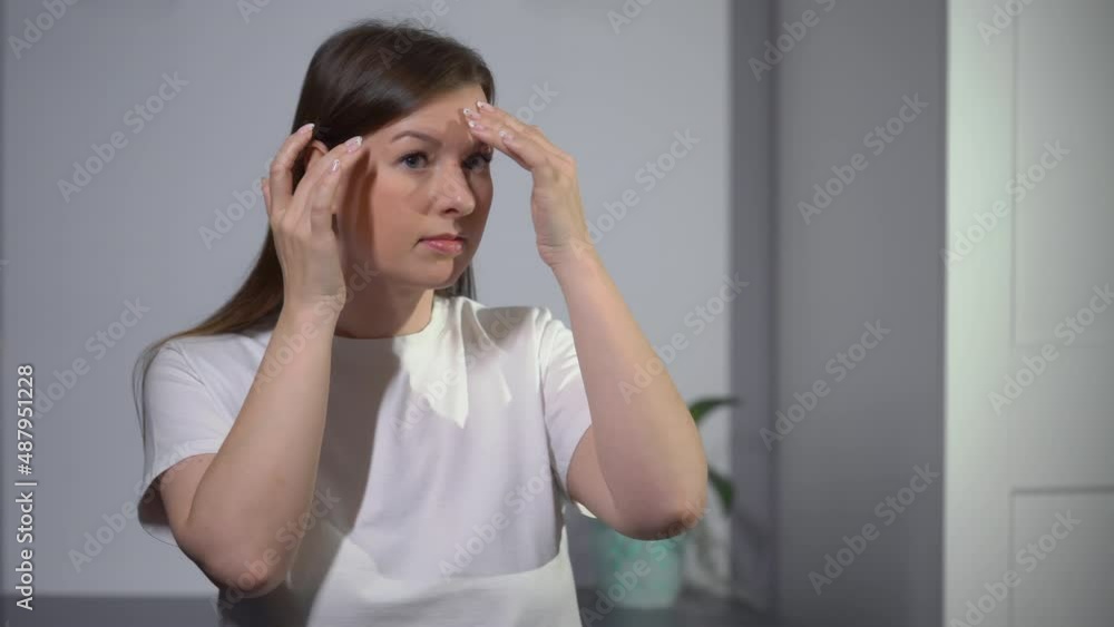 A young woman looks in the mirror. Beautiful girl is going, looking at skin. 