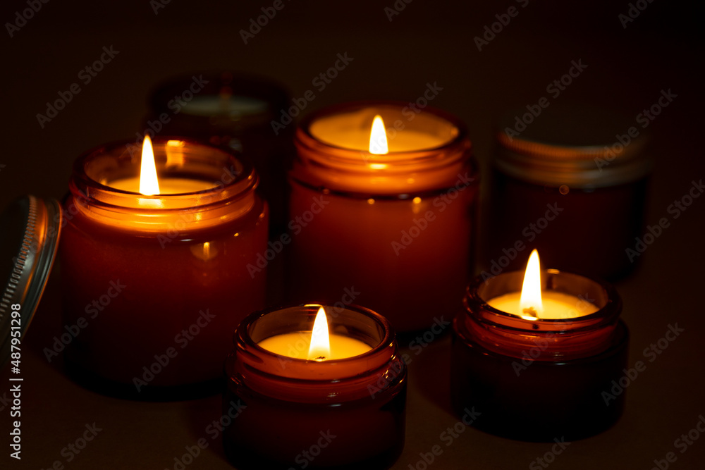 A set of different aroma candles in brown glass jars. Scented handmade candle. Soy candles are burning in a jar at night. Aromatherapy and relax in spa and home. A set of different aroma candles in brown glass jars. Scented handmade candle. Soy candles are burning in a jar at night. Aromatherapy and relax in spa and home.