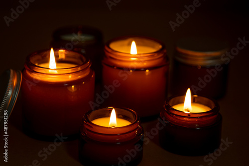 A set of different aroma candles in brown glass jars. Scented handmade candle. Soy candles are burning in a jar at night. Aromatherapy and relax in spa and home.