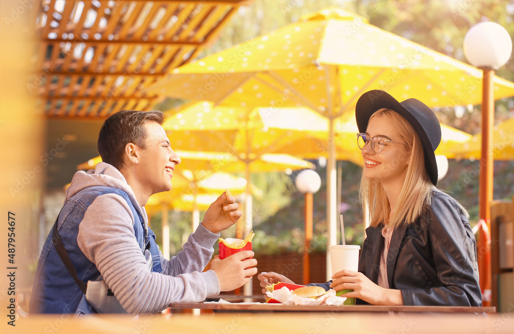 Young couple eating french fries in cafe outdoors Young couple eating french fries in cafe outdoors
