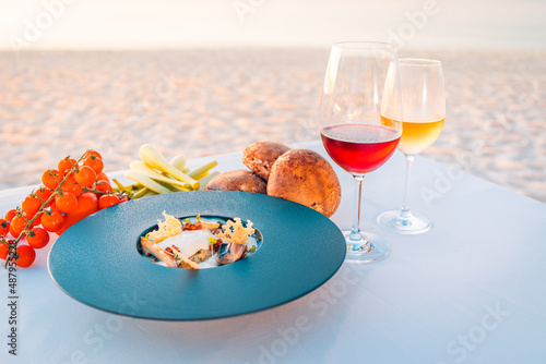 Sunset appetizer with wines and fresh vegetables on beach dinner table. Luxury food background, destination dining closeup. 