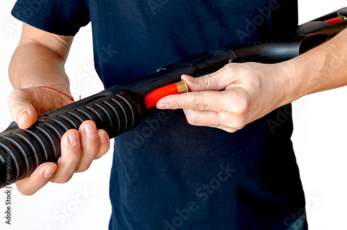 Close up of man loading a red shotgun shell into the magazine of his weapon