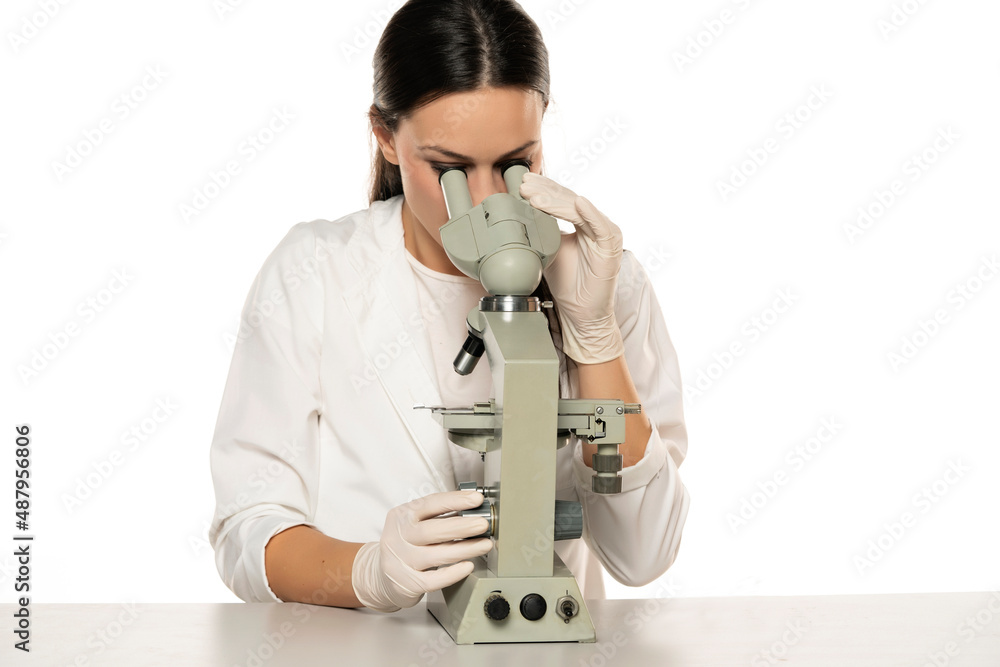 a young female scientist looks through a microscope in a studio on a white a young female scientist looks through a microscope in a studio on a white