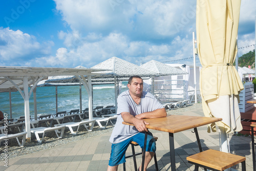 40-year-old man sits at an empty table on the seashore, an empty beach. Summer vacation