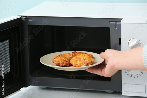 Woman putting plate with food into microwave oven, closeup