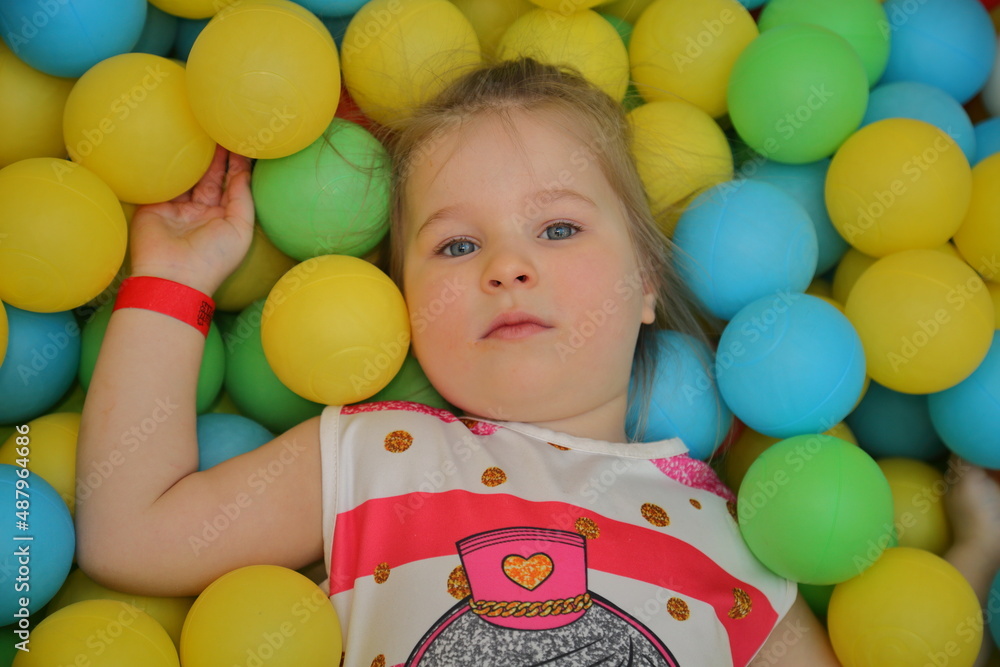 Obraz premium A cheerful girl is playing in the playroom in the pool with balls of different colors