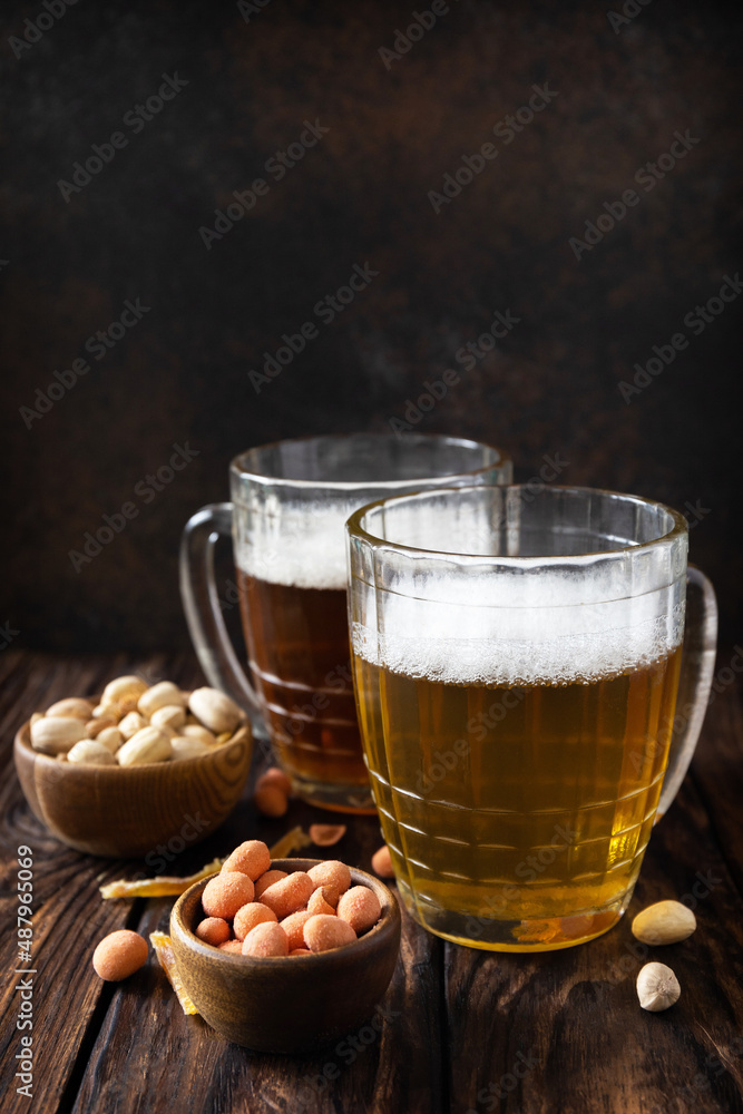 Alcohol drink pint of lager and pint of stout, craft beer. Two Glass of Beer with foam and snacks on a wooden rustic background. Traditional German wheat beer. Copy space. Alcohol drink pint of lager and pint of stout, craft beer. Two Glass of Beer with foam and snacks on a wooden rustic background. Traditional German wheat beer. Copy space.