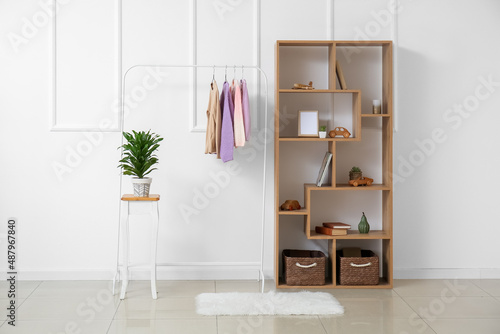 Rack with children's sweaters and shelf unit near light wall in room interior
