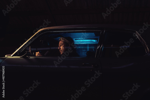Man with blond hair sits inside an American classic muscle car at night.