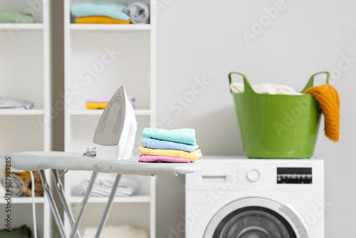 Electric iron and stack of clean clothes on board in laundry room