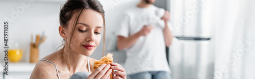 young woman holding croissant near blurred man on background  banner.