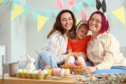 Young lesbian couple with little daughter during painting of Easter eggs at home