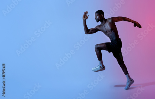 Full length portrait of focused young black man with bare torso running fast in neon lighting, copy space