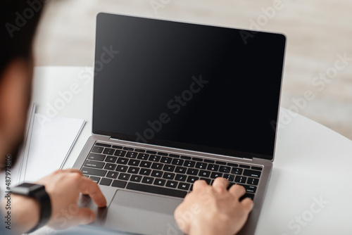 Lifestyle and gadgets concept. Unrecognizable adult man using laptop with blank black screen for mockup template