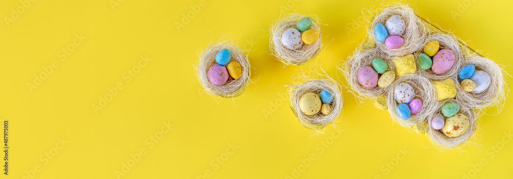 Happy Easter concept. Sweet bright easter eggs in nests on yellow background