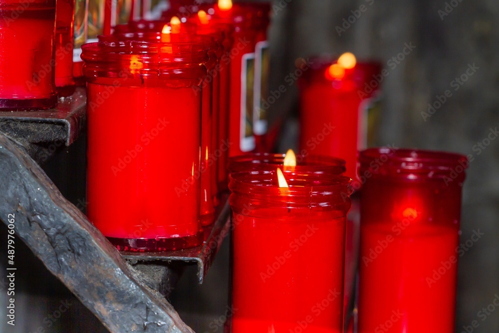 Red candles in church in foreground on iron display stand, religion concept.