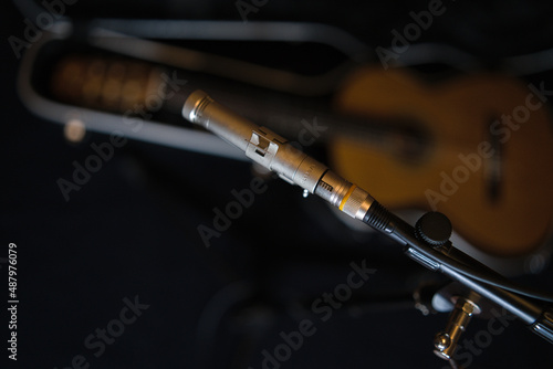 Musical accessories. A condenser microphone on a stand against the background of a guitar in an open trunk.