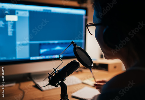 Microphone with pop filter closeup photo with a young woman in headphones recording voice using a desktop computer with music creation studio app. Modern home sound studio audio recording technology. photo