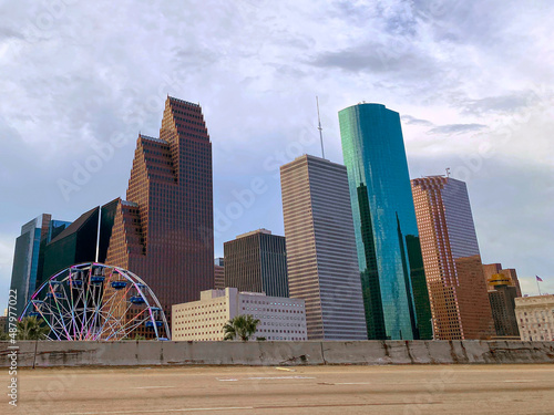 Downtown Houston skyline and skyscrapers in a gray-ish blue hue on a cloudy day with a lighted ferris wheel in the forefront taken from the freeway, driver POV, empty freeway