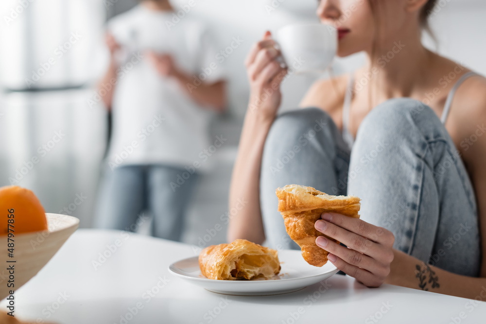 cropped view of tattooed woman drinking coffee and holding croissant. cropped view of tattooed woman drinking coffee and holding croissant.