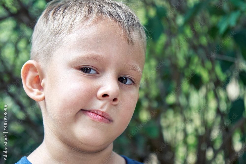 Blond preschooler grimaces making weird face expressions. Boy has fun walking outdoors in shade of trees in park on summer holiday closeup Blond preschooler grimaces making weird face expressions. Boy has fun walking outdoors in shade of trees in park on summer holiday closeup