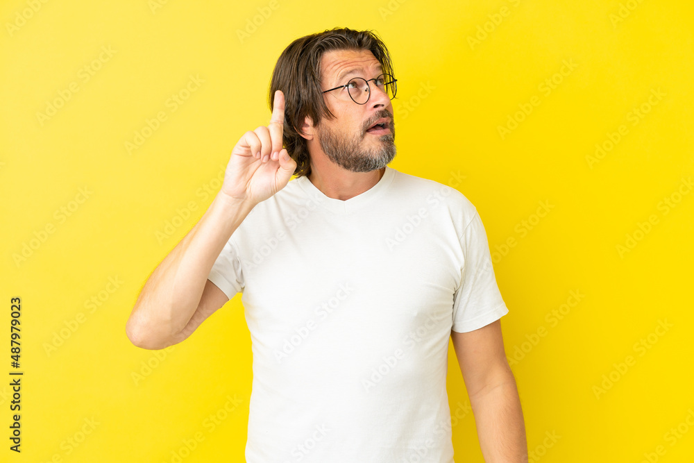 Senior dutch man isolated on yellow background intending to realizes the solution while lifting a finger up Senior dutch man isolated on yellow background intending to realizes the solution while lifting a finger up