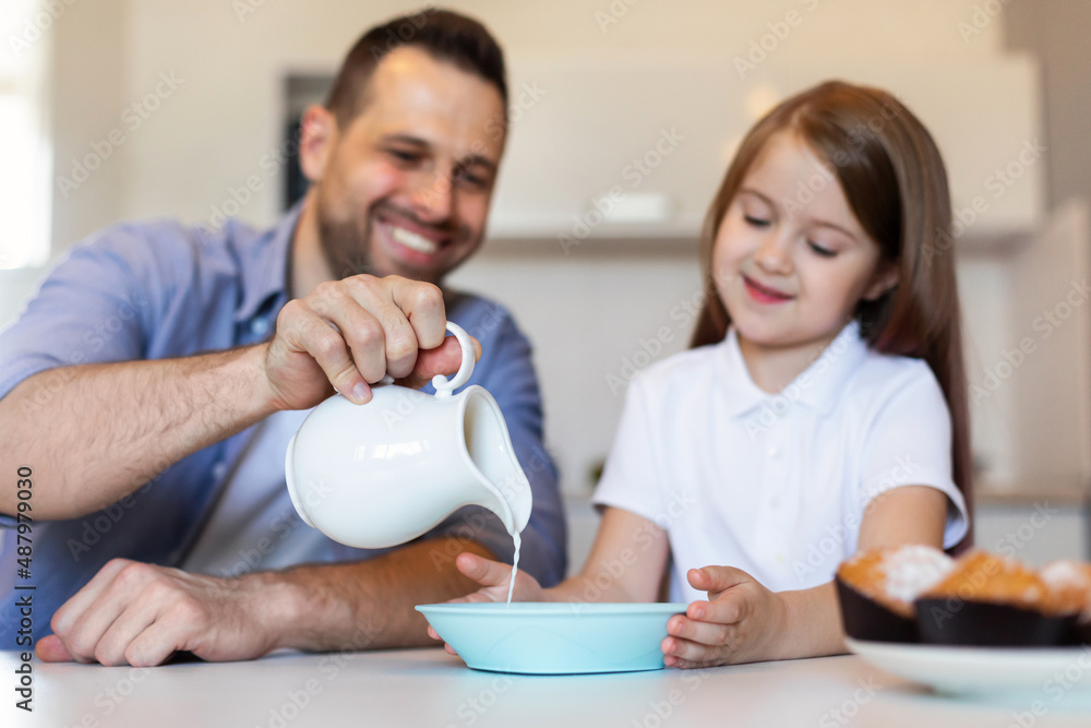 Dad And Daughter Having Breakfast Adding Milk To Cereal Indoor Dad And Daughter Having Breakfast Adding Milk To Cereal Indoor