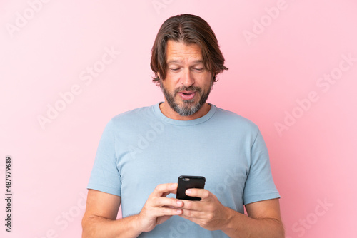 Senior dutch man isolated on pink background sending a message or email with the mobile © luismolinero
