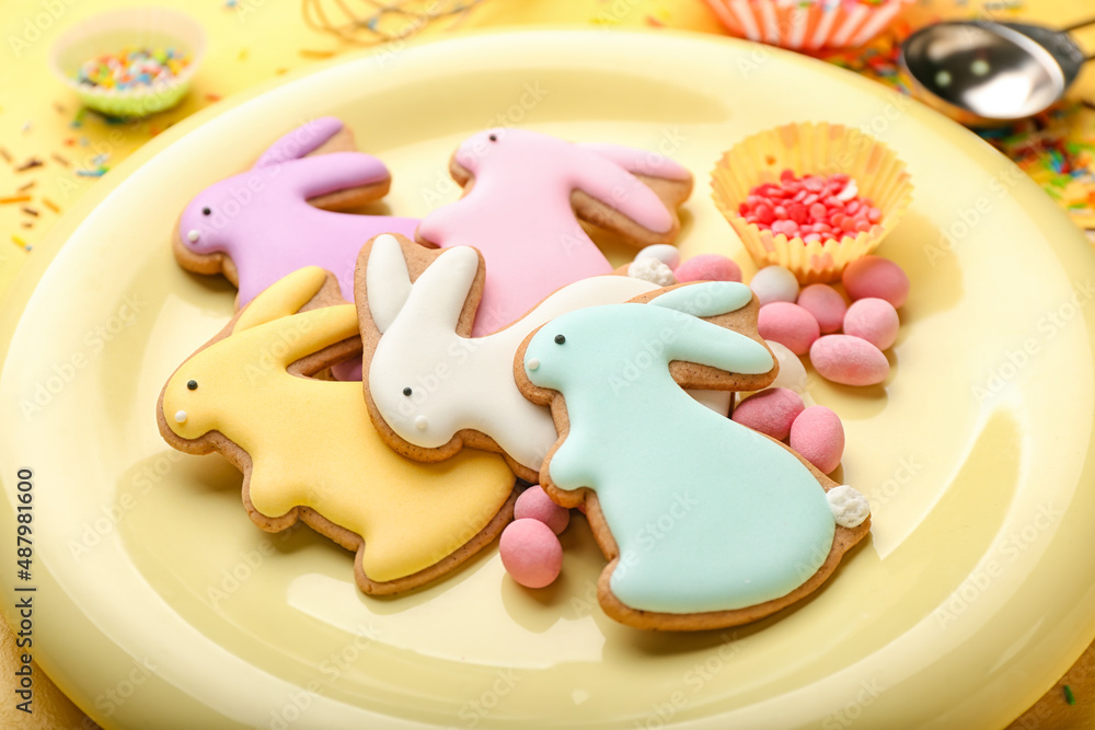 Plate with tasty Easter cookies in shape on bunny and candies on table, closeup