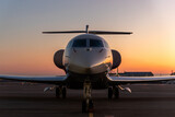 Scenic front view modern luxury expensive private jet plane parked airport taxiway hangar warm colorful dramatic evening warm sunset sun light sky background. Executive aicraft vip travel concept