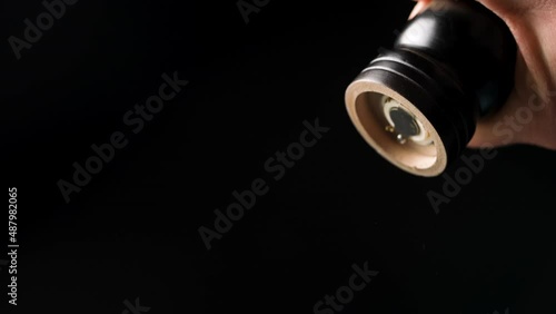Male chef grinding pepper or spices on isolated black background restaurant kitchen. Chef's hands grinding spicing with a hand pepper mill. Slow motion of spicy condiment falling. Close up.