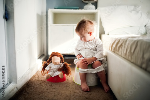 Cute caucasian kid with doll sit on potty in bedroom, concept of hygiene and potty training photo