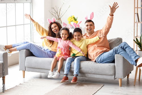 Little children with Easter rabbits and their parents sitting on sofa at home